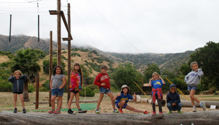 kid posing for a photo on top of a log by the ropes course